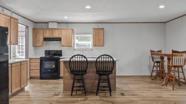Una cocina con armarios de madera, una estufa negra, dos taburetes negros y una mesa de comedor de madera con sillas.