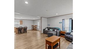 Un salón amplio con suelo de madera, un sofá gris, una mesa de centro de madera y un comedor con mesa y sillas.