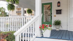 A white porch with blue steps, a green door, and hanging plants.