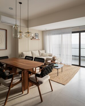 Ein modernes Wohnzimmer mit einem Holzesstisch, schwarzen Stühlen, einem weißen Sofa und einem großen Fenster mit durchsichtigen Vorhängen.