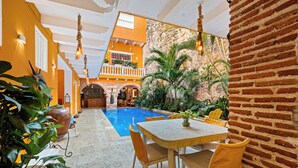 Un área de piscina con mesa y sillas, rodeada de plantas y un muro de ladrillo.