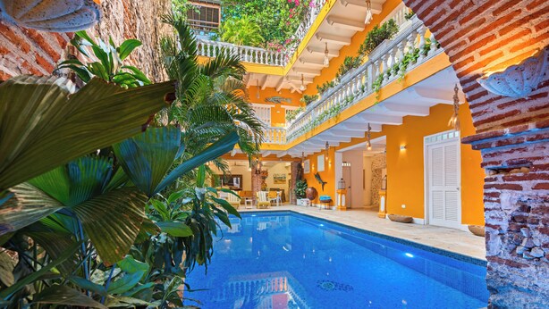 Piscina interior con pared de ladrillo y plantas tropicales.