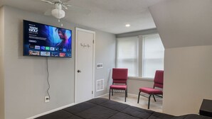 Un dormitorio con una cama grande, un televisor montado en la pared, dos sillones rojos y una puerta con un cartel.