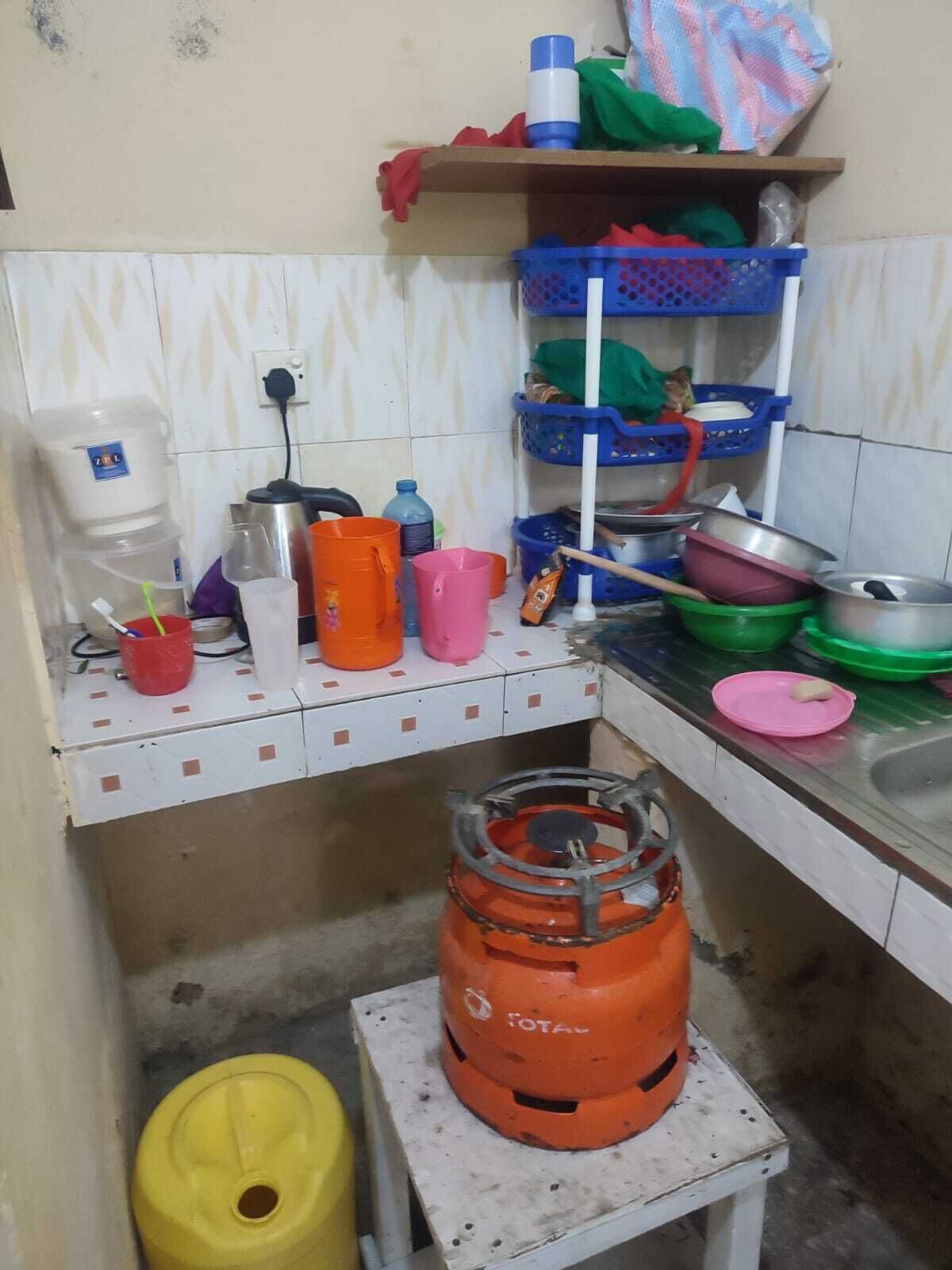 Una cocina pequeña con dispensador de agua, cilindro de gas y diversos utensilios y recipientes de cocina.
