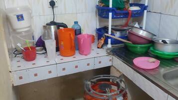 Una cocina pequeña con dispensador de agua, cilindro de gas y diversos utensilios y recipientes de cocina.