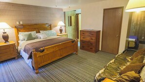 Une chambre d’hôtel avec un lit en bois, deux tables de chevet avec des lampes, une commode, une porte et un tapis à motifs.