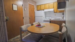 Une cuisine compacte équipée d’une cuisinière, d’un évier et de meubles de rangement en bois. On y trouve une table à manger avec des chaises et un petit tapis.