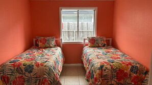 Habitación con dos camas, cada una con ropa de cama floral, una ventana con persianas y paredes color naranja.