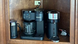 Un armario de madera con tres máquinas de café: una Keurig, una Nespresso y un Longines.