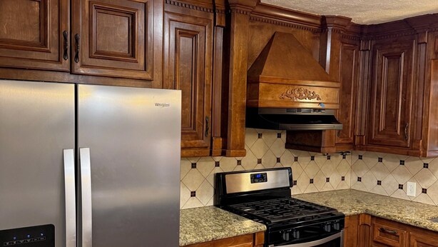 Una cocina con armarios de madera, un refrigerador de acero inoxidable, una estufa a gas y un horno empotrado.