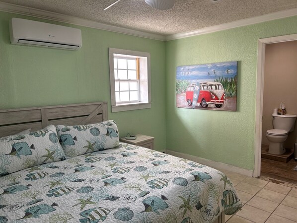 A bedroom with a bed, a window, an air conditioner, a painting, and a toilet. - 3-bedroom house in Galveston, no stairs for relaxing stay.  2 blocks from beach! (Galveston)