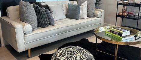 Un salon moderne avec un canapé blanc, un pouf noir et blanc à motifs et une table basse sur laquelle sont posés des livres.