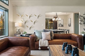 Ein modernes Wohnzimmer mit einem braunen Ledersofa, einem Couchtisch mit Kameras und einer Wand, die mit Kuhskulpturen verziert ist.