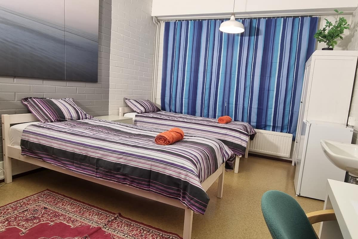 Een slaapkamer met twee bedden, een bureau, een stoel, een wastafel en een spiegel.
