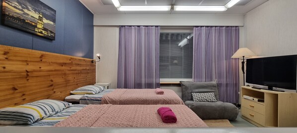 A hotel room with two beds, a TV, a sofa, and a window with curtains.
