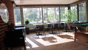A sunlit room with a pool table, chairs, and a sign indicating a hostel lounge.