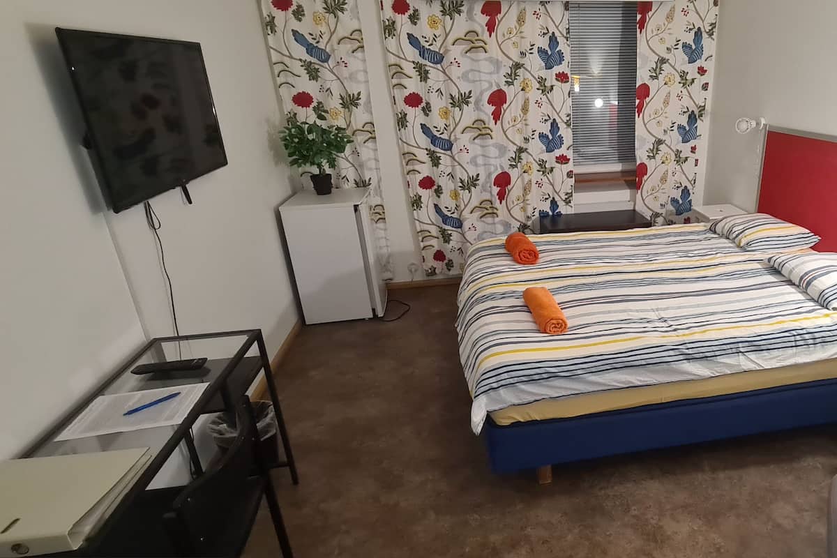 Een slaapkamer met een bed, een bureau, een stoel, een televisie en een lamp.
