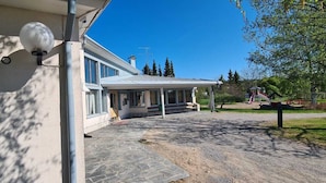 A building with a sign reading "KIRJASTO" and a covered outdoor area with a paved walkway.