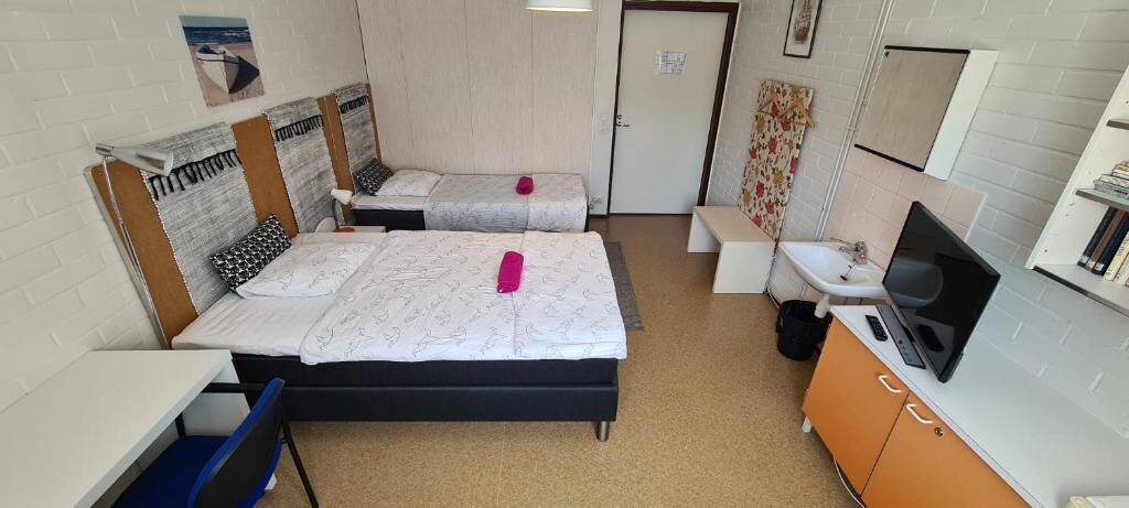A room with two beds, a desk, a chair, a TV, and a small bathroom.