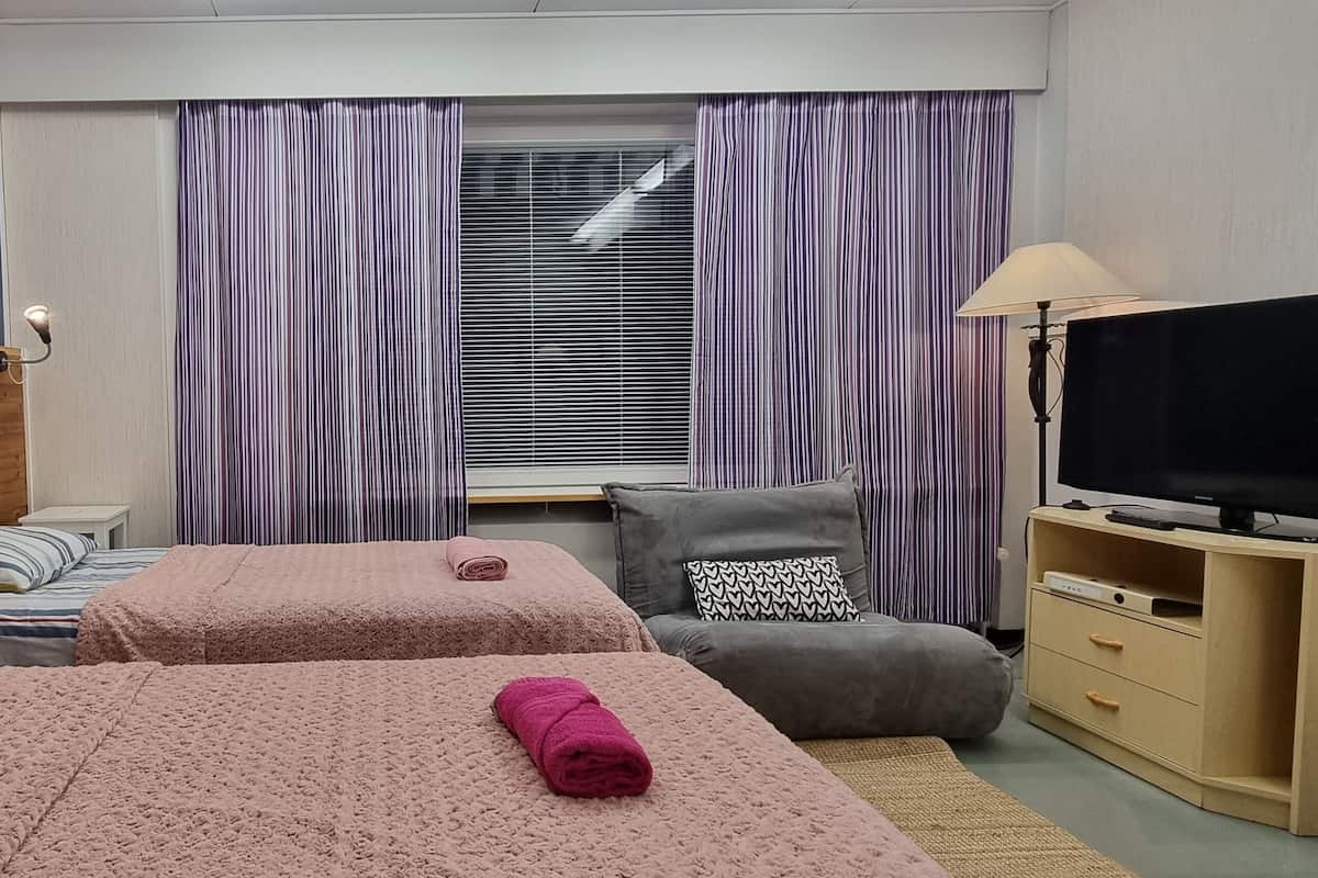 Een hotelkamer met twee bedden, een televisie, een bureau en een raam met gordijnen.