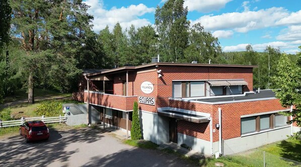 A brick building with a sign reading "ECURAS" and a parking area with a red car. - Majatalo Villanen (Längelmäki)