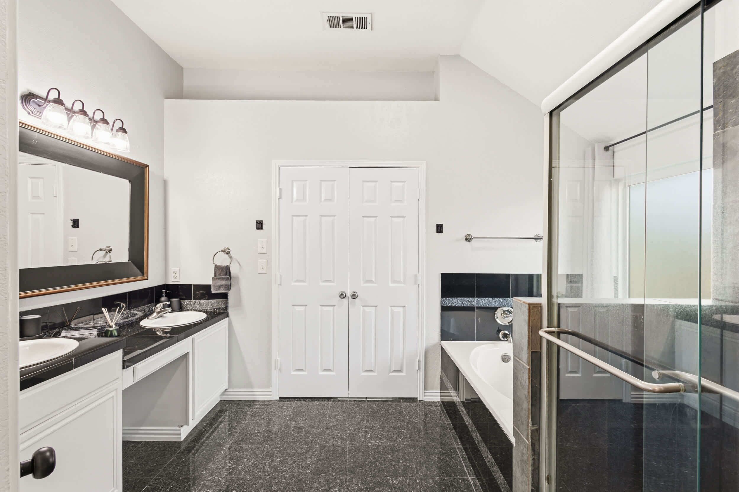 A modern bathroom with a large mirror, two sinks, a bathtub, and a glass shower enclosure.