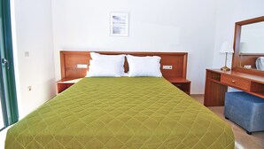 Ein Hotelzimmer mit einem Bett, einem Nachttisch aus Holz, einem Schreibtisch mit Stuhl, einem Spiegel und einem Bild an der Wand.