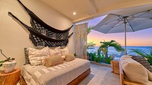 A bedroom with a bed, a hammock, a view of the ocean, and a balcony with plants. - New 4BR Luxury Condo at Indah (Puerto Vallarta)
