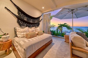 Ein Schlafzimmer mit Bett, einer Hängematte, Meerblick und einem Balkon mit Pflanzen.