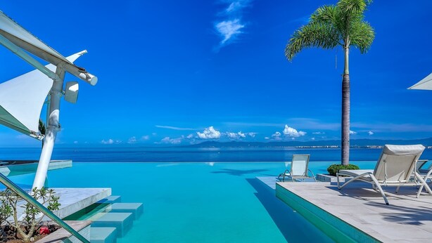 A clear blue pool with steps leading to a lounge area with chairs and a palm tree. - New 4BR Luxury Condo at Indah (Puerto Vallarta)