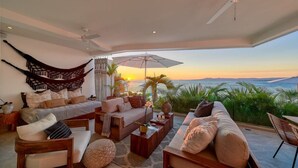A spacious living area with a large bed, sofas, and a view of the ocean at sunset. - New 4BR Luxury Condo at Indah (Puerto Vallarta)
