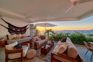 Ein geräumiger Wohnbereich mit einem großen Bett, Sofas und Blick auf den Sonnenuntergang über dem Meer.