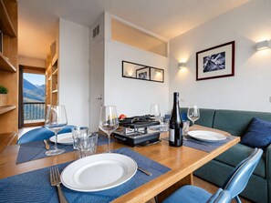 A dining area with a table set for two, a bottle of wine, and a view of the mountains through a window. - Ski-In/Out Apt w/ Mountain View (Val Thorens)
