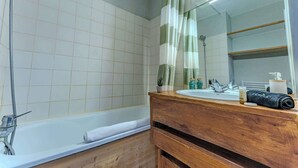 A bathroom with a bathtub, a wooden vanity, a mirror, and a shower curtain. - Alpine Ski-In/Out w/MountainView (Val Thorens)