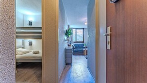 A narrow hallway leading to a bedroom with bunk beds, a small kitchenette, and a living area with a sofa and a plant. - Alpine Ski-In/Out w/MountainView (Val Thorens)