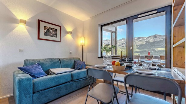Ein modernes Wohnzimmer mit Sofa, Esstisch, Stühlen und einem großen Fenster mit Blick auf die Berge.