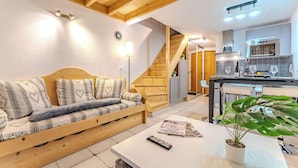 A cozy living room with a wooden sofa, a coffee table, and a staircase leading to a kitchen area. - Mountain Hideaway near the Slope (Val Thorens)