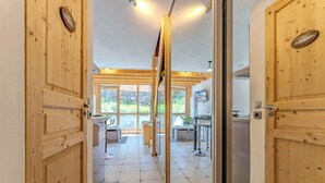 A wooden interior with a kitchen and dining area, featuring large windows and a stone wall visible through the glass doors. - Mountain Hideaway near the Slope (Val Thorens)