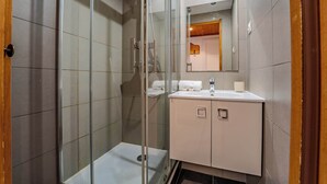 Um banheiro moderno com chuveiro em box de vidro, toucador branco com espelho e paredes revestidas de azulejo.