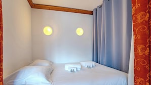 Cama bem arrumada com lençóis brancos, duas luminárias de cabeceira e uma cortina.