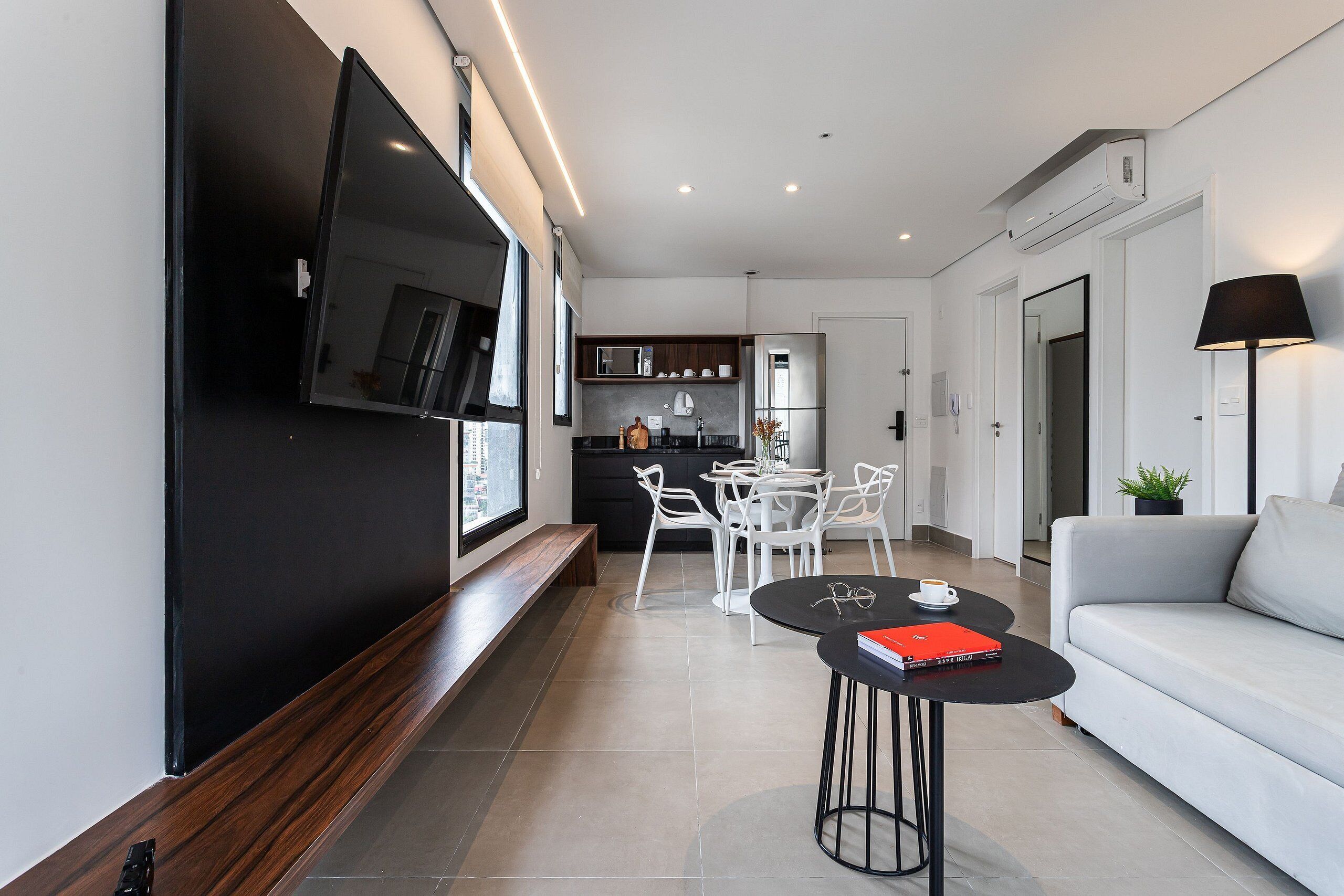 A modern living room with a flat-screen TV, a sofa, a dining area with chairs, and a kitchen in the background.