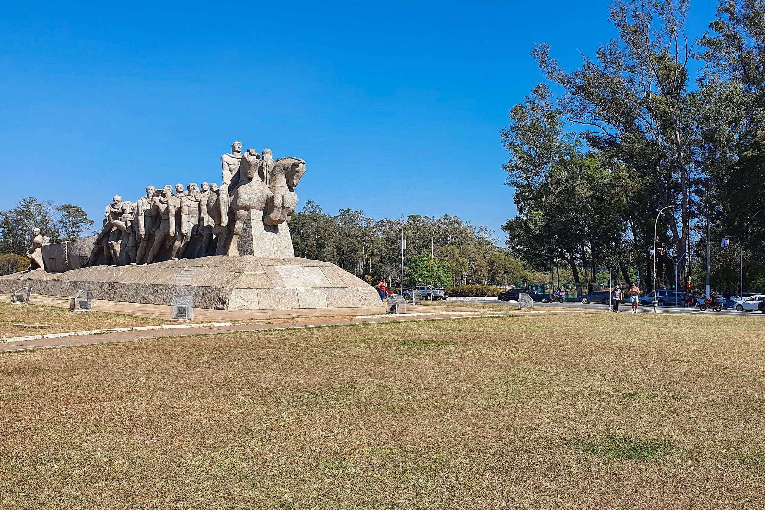 A large outdoor sculpture with multiple figures, surrounded by a grassy area and trees.