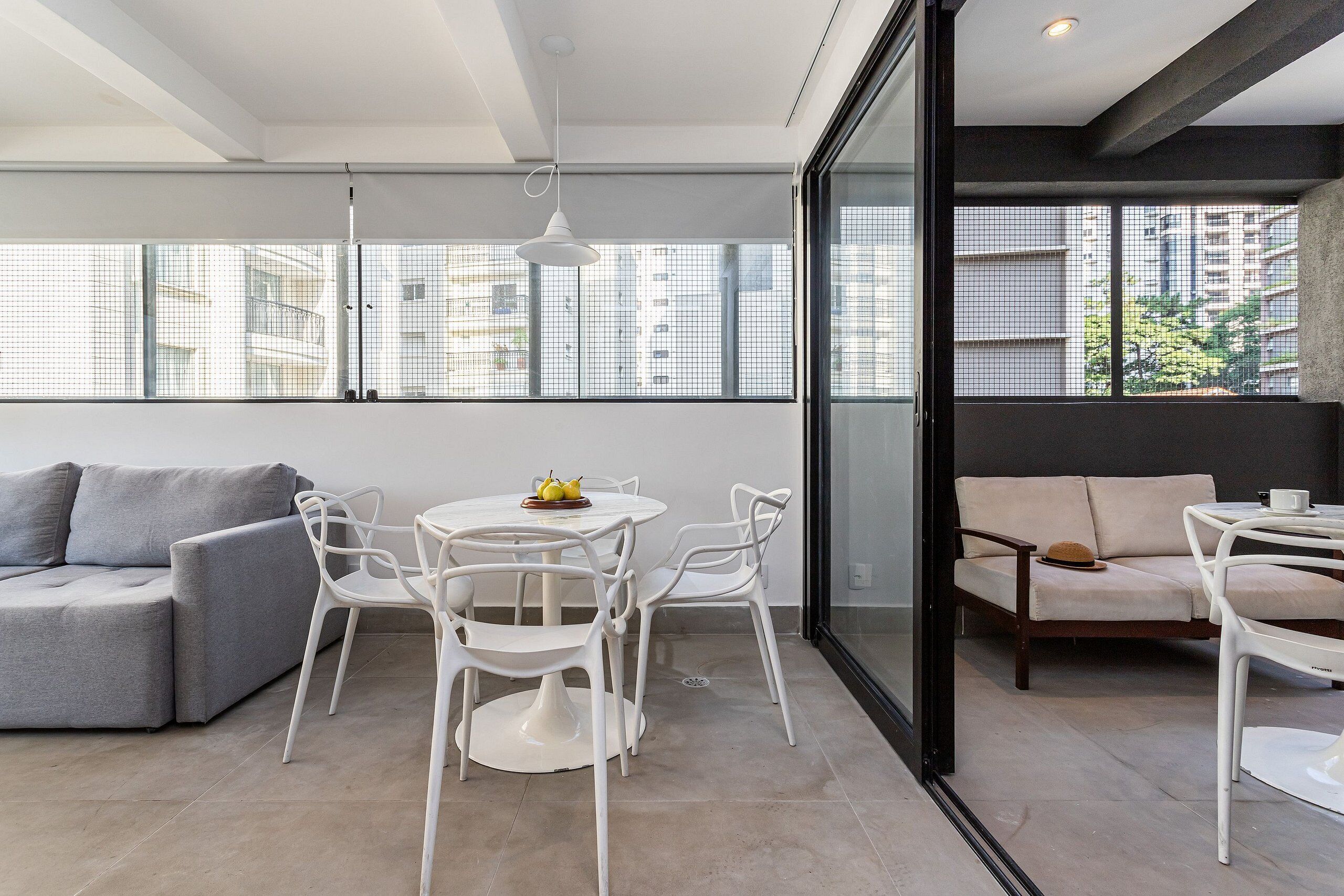 A modern interior with a grey sofa, white chairs, a round table, and a glass partition.