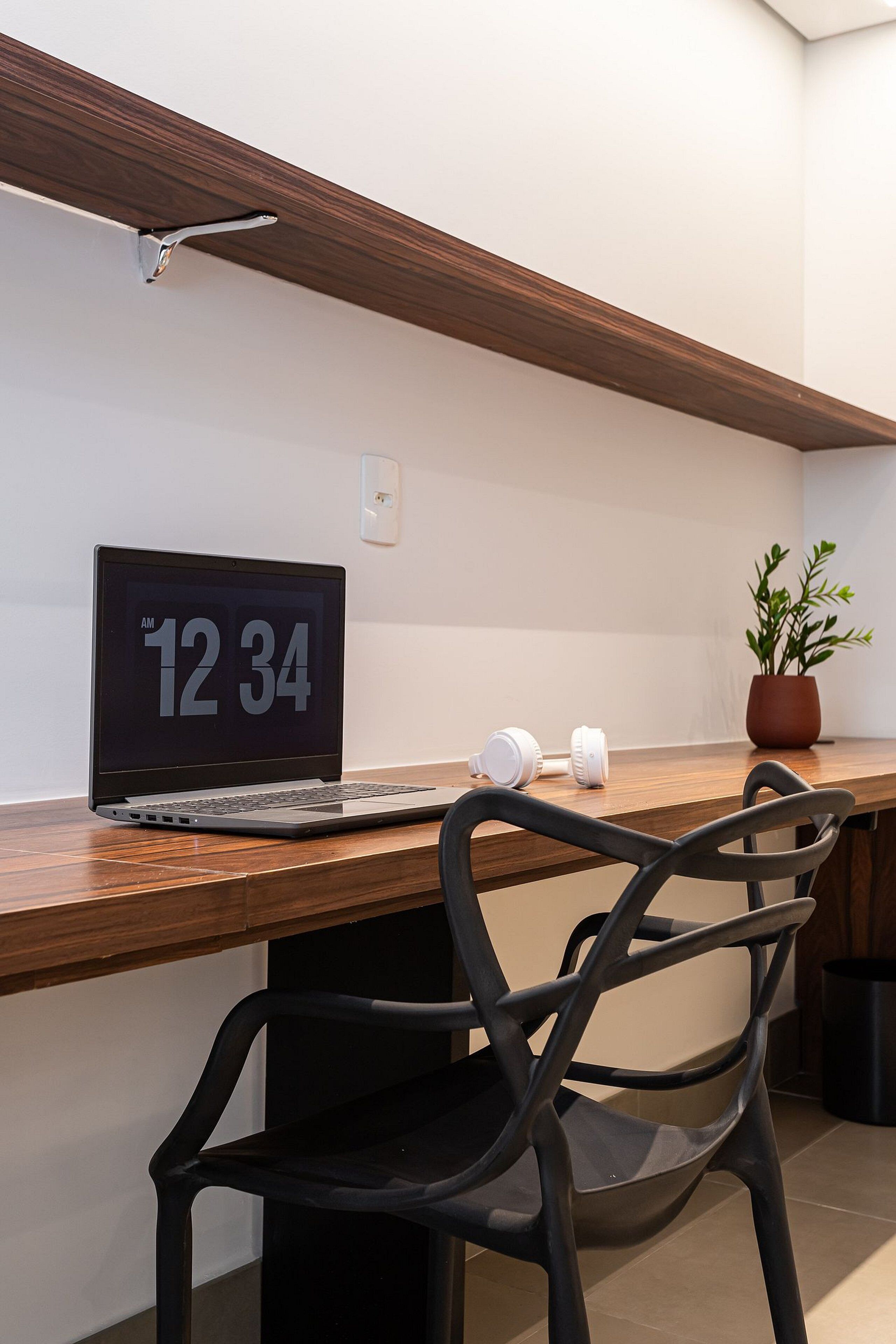 A wooden desk with a laptop displaying the time, a potted plant, and a black chair.