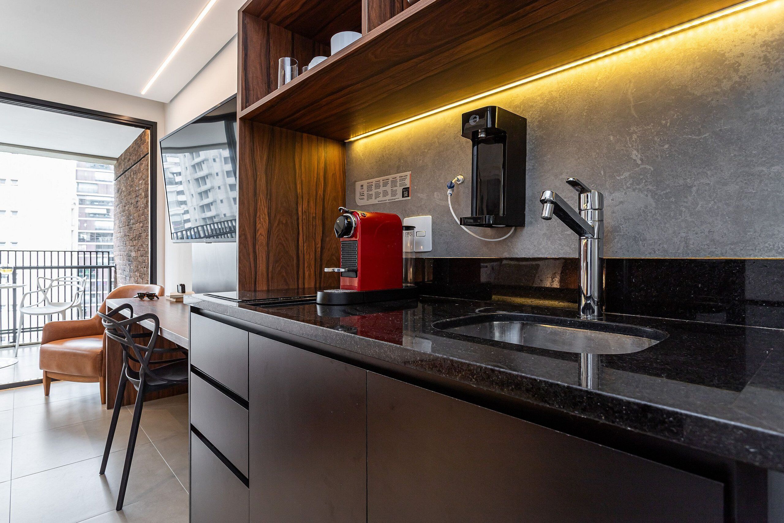 Cocina moderna con cafetera integrada, un lavamanos y una zona de comedor con una silla y una mesa.