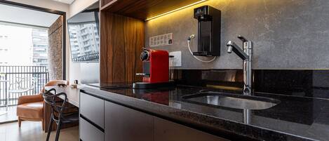 Cocina moderna con cafetera integrada, un lavamanos y una zona de comedor con una silla y una mesa.