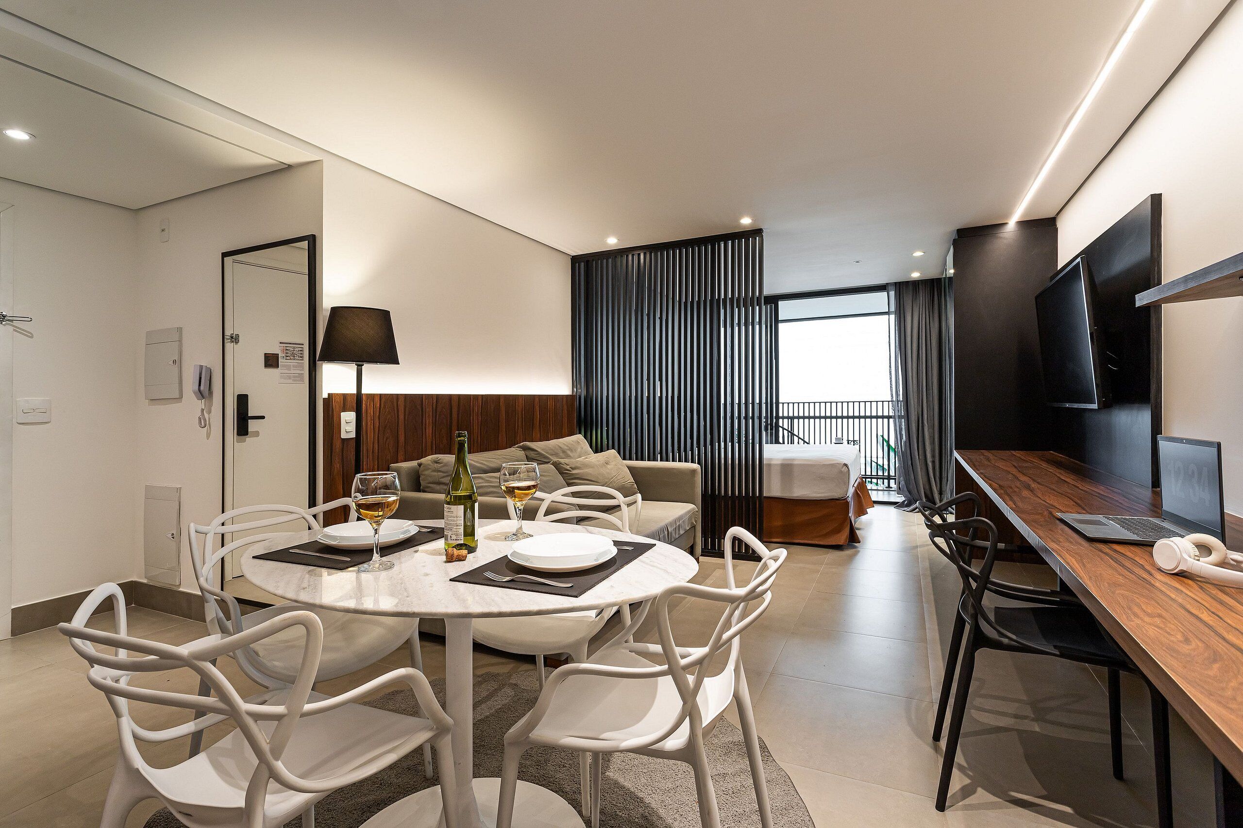 A modern hotel room with a dining area, a sofa, a TV, and a balcony with curtains.