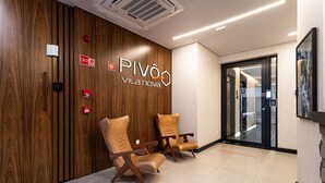 A reception area with a wooden wall, two leather chairs, a glass door, and a sign reading 'PIVO VILA nova'. - Pivô Vila Nova by Viva - Conforto e Localização Privilegiada (São Paulo)