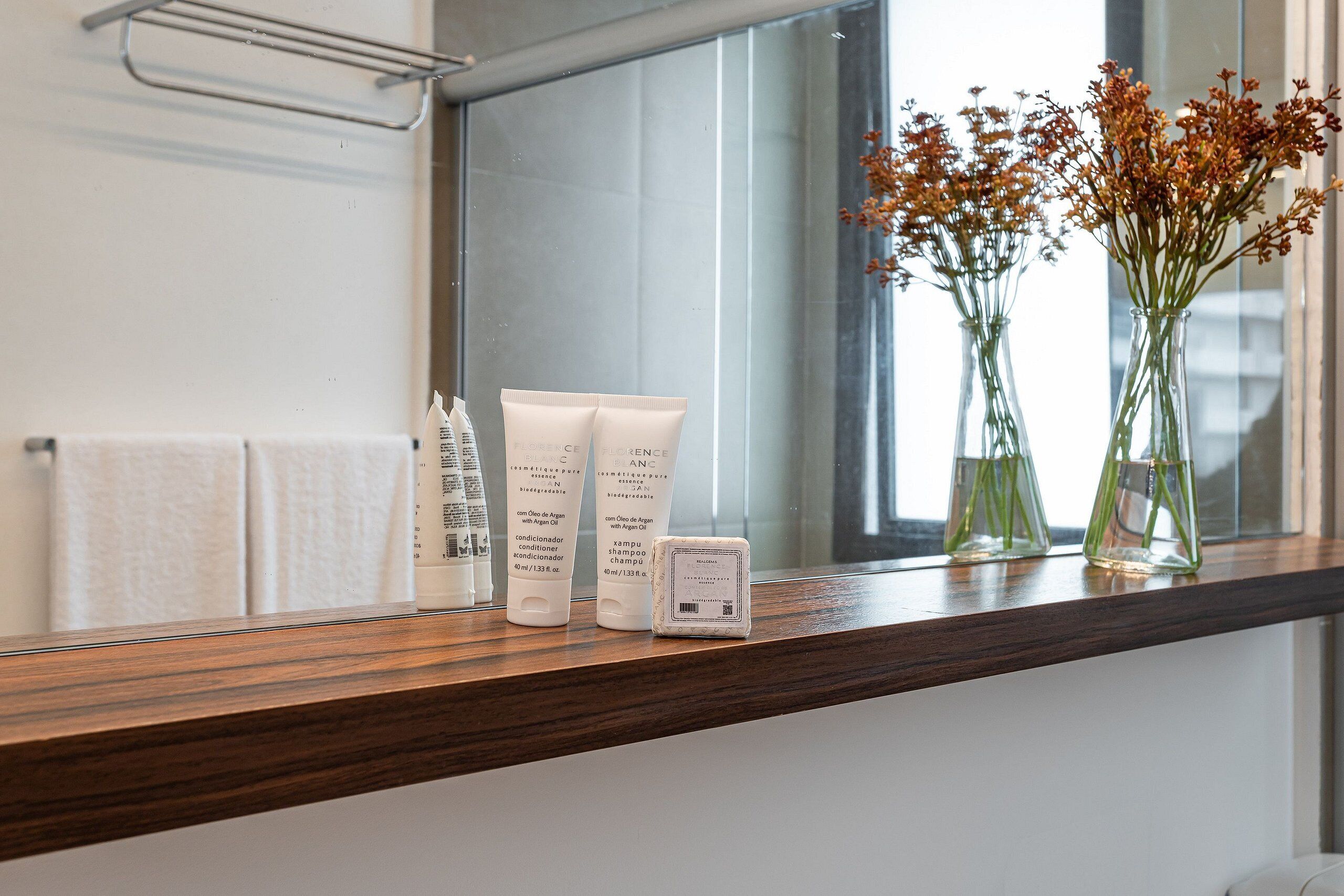 A bathroom vanity with toiletries, a mirror, and a window with flowers.
