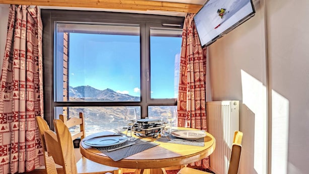 A dining area with a table set for two, a window with a mountain view, and a television mounted on the wall. - Mountain-View with Ski-In ski Out Stay (Val Thorens)